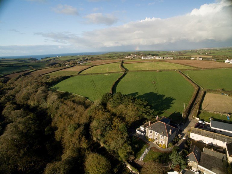 Aerial view of Nanplough Farm with green fields rolling towards the Cornish coast